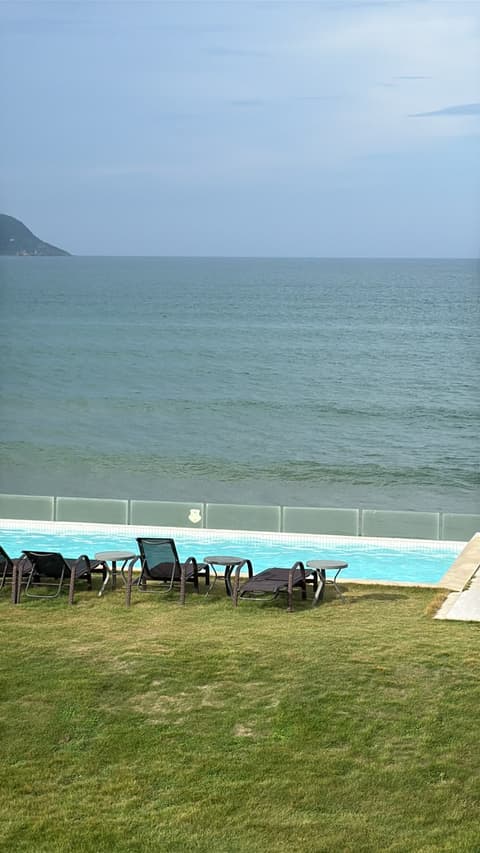 Piscina de frente para o mar, com espreguiçadeiras sobre o gramado.